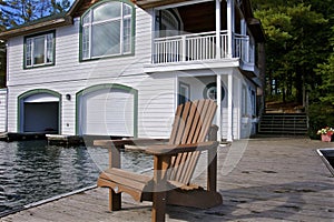 A Muskoka chair sitting on a wood dock facing a calm lake.  Pier for boat and balcony for a vista of the lake