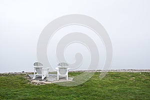 Muskoka chairs on the lake front with white sky