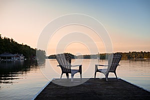 Muskoka chairs sitting at the end of a dock in front of Lake Joseph at sunrise.