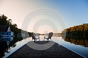 Muskoka chairs sitting at the end of a dock in front of Lake Joseph at sunrise.