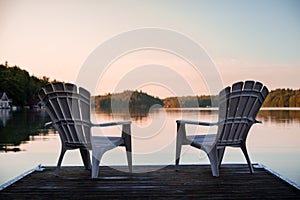 Muskoka chairs sitting at the end of a dock in front of Lake Joseph at sunrise.