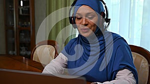 Muslim Arab beautiful woman in hijab, call center operator works with headset communicates by video link, using laptop