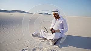 Muslim Arabian UAE Sheikh architect sitting with laptop on sand