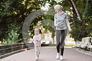 Muslim Arabian woman enjoying running together in park with her cute active 4-aged daughter