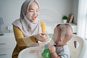 Mother feeding her baby boy while sitting on high chair