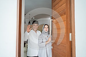 muslim asian senior couple standing at front door waiting for family