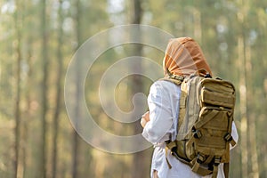 Muslim Asian woman wearing hijab with a backpack and hat hiking in the mountains during the summer season