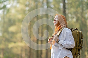 Muslim Asian woman wearing hijab with a backpack and hat hiking in the mountains during the summer season