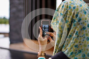 A muslim Asian woman wearing hijab taking picture with smartphone