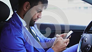 Muslim businessman sitting in the car and typing on the smartphone