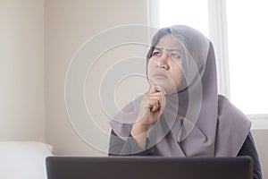 Muslim Businesswoman Working on Laptop at Home, Thinking Gesture