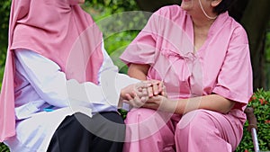 Muslim careful caregiver or doctor hold the patient hand and encourage the patient in a wheelchair. Concept of happy retirement