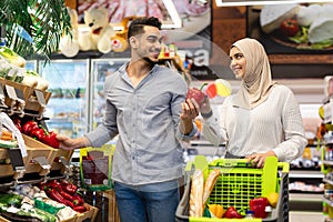 Muslim Couple Enjoying Grocery Shopping Together Buying Vegetables In Supermarket