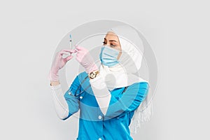Muslim doctor or nurse in hijab and medical face mask holding a syringe on a gray background. the concept of vaccination of the