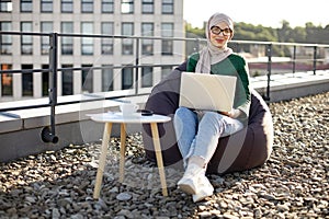 Muslim employee with gadget doing remote job on rooftop