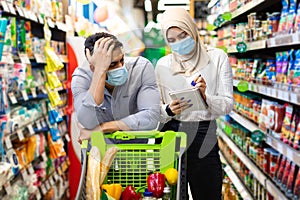 Muslim Family Couple Calculating Prices On Grocery Shopping In Supermarket