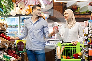 Muslim Family Couple On Grocery Shopping Choosing Vegetables In Supermarket
