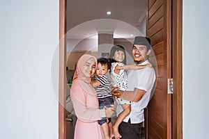 muslim family standing in front of their front door house welcoming guest at home