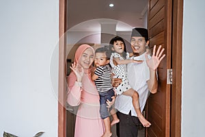 muslim family standing in front of their front door house welcoming guest at home