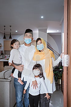 muslim family standing with mask in front of their front door house welcoming guest at home
