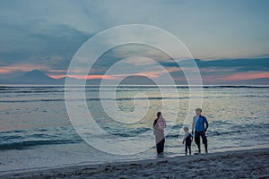 Muslim family walking along the beach in the sunset