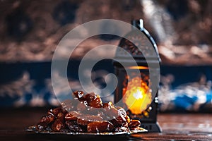 The Muslim feast of the holy month of Ramadan Kareem. Beautiful background with a shining lantern Fanus and dried dates on wooden