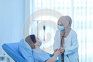 Muslim female doctor holding hand of the elderly patient sitting on the bed at hospital, takes care and cheerful concept