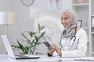 Muslim female doctor smiles using smartphone in clinic