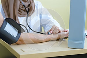 Muslim female doctor using sphygmomanometer with stethoscope checking blood pressure to patient in the hospital