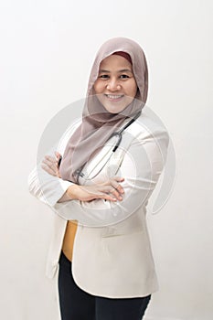 Muslim female doctor wearing hijab and suit, standing with crossed arm and holding stethoscope, succesful confident person