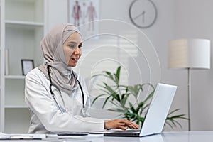 Muslim female doctor working on laptop in clinic office