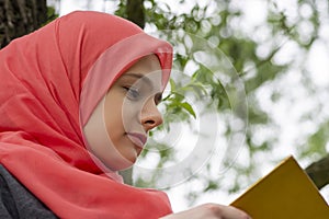 Muslim female student reading a book in nature, outdoor