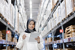 Muslim female wearing hijab warehouse worker holding tablet checks stock on shelf storehouse. businesswoman islamic entrepreneurs