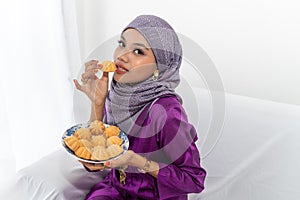 Muslim girl celebrates end of Ramadan, in purple dress, and holding food, portrait waist up