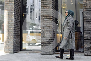 Muslim girl in a green hijab and sunglasses walking on the street