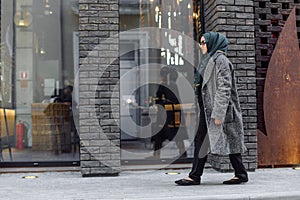 Muslim girl in a green hijab and sunglasses walking on the street