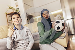 Muslim girl and her caucasian  friend are watching a football match at home