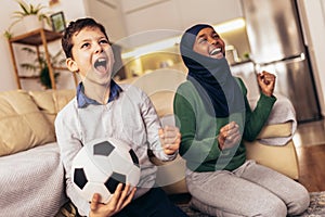 Muslim girl and her caucasian  friend are watching a football match at home