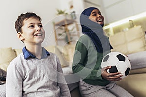 Muslim girl and her caucasian  friend are watching a football match at home