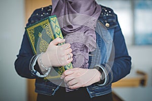 Muslim girl with a purple hijab holding a Kuran with her right hand