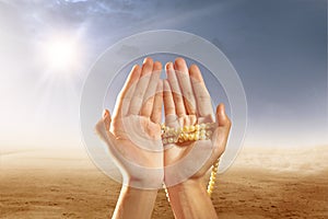 Muslim hands praying with prayer beads on desert