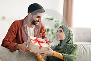 Muslim Husband Giving Present Box To Happy Wife Sitting Indoors