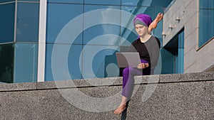 Muslim islamic indian woman in hijab girl yogi female gymnast sitting in city with laptop working online holding leg