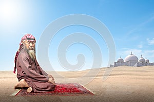 Muslim man with a beard wearing keffiyeh with agal in praying position (salat) on the prayer rug photo