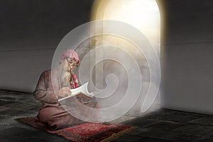 Muslim man with a beard wearing keffiyeh with agal sitting and reading the Quran