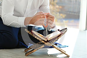 Muslim man with Koran and misbaha praying indoors