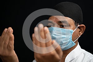 Muslim man in medical mask preforming Salah or prayer by closing eyes.