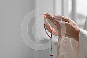 Muslim man with misbaha praying indoors, closeup. Space for text