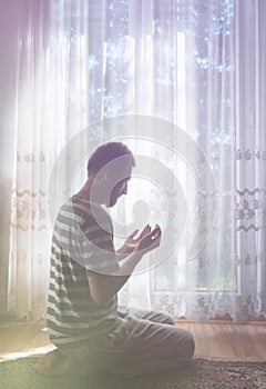 Muslim man praying indoor at dark room with bright window light