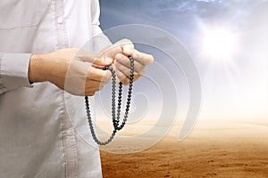 Muslim man praying with prayer beads on his hands on desert
